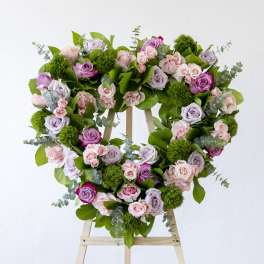 Heart-shaped floral wreath of pink and lavender roses on a wooden stand
