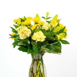 Yellow carnations, chrysanthemums, and lilies arranged in a clear glass vase