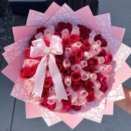 Bouquet of red and pink roses wrapped in pink paper with a white bow