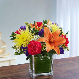 Colorful bouquet with orange lilies, yellow daisies, and pink carnations in a glass vase