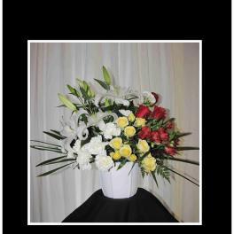 White vase arrangement with lilies, roses, carnations, and red flowers