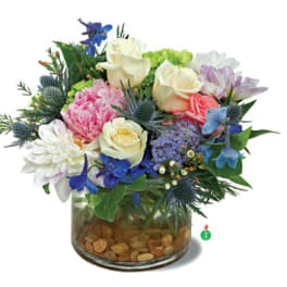Low glass vase filled with cream roses, pink peony, blue and purple blooms, and mixed pastel flowers.