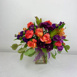 Mixed bouquet of purple, coral, and orange flowers in a glass vase