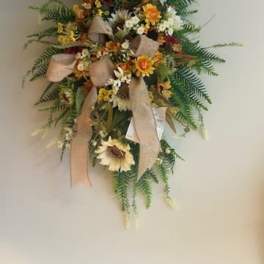 Wall-mounted floral spray with sunflowers, white blooms, and beige ribbons