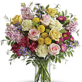 Mixed bouquet of pink and yellow roses with carnations and pompons in a clear glass vase