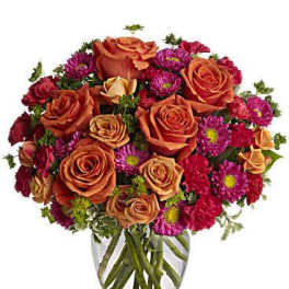 Orange roses and magenta daisies in a clear glass vase
