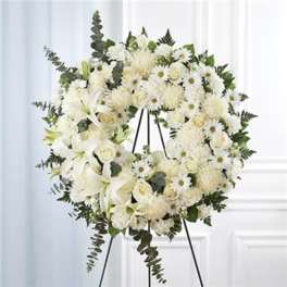White funeral wreath on a black easel with lilies, roses, and daisies