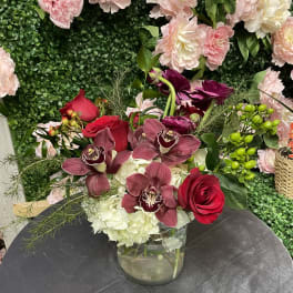 Mixed bouquet in a clear glass vase with red roses and burgundy orchids