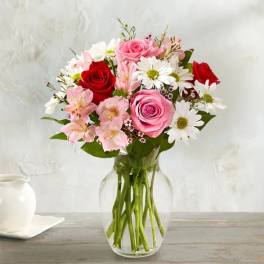 Bouquet of pink and red roses with white daisies in a clear glass vase