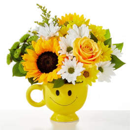 Yellow mug vase holding sunflowers, daisies, and a rose