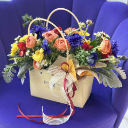 Mixed bouquet in a beige gift bag with peach, yellow, red, and blue flowers