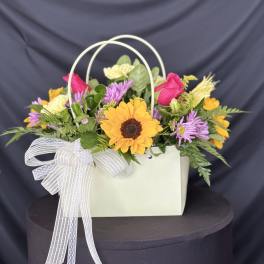 Mixed flower arrangement in a white handled gift bag with a ribbon bow