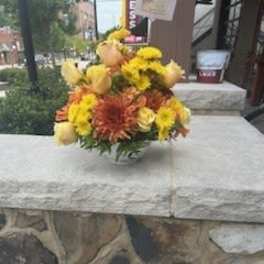 Yellow and orange flower arrangement in a clear vase on a stone table