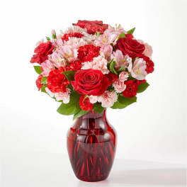 Bouquet of red roses, pink alstroemeria, and carnations in a red glass vase