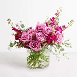 Pink roses and magenta flowers arranged in a clear glass vase