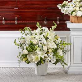 White funeral arrangement in a vase beside a casket