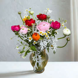 Tall mixed bouquet of pink, red, white, and orange ranunculus with small daisies in a green glass vase