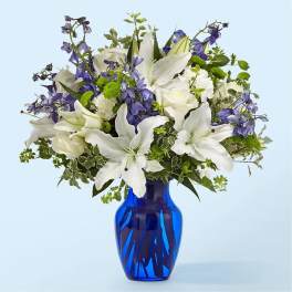 White lilies and purple flowers in a blue glass vase