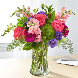 Mixed bouquet of pink, purple, and white flowers in a clear glass vase