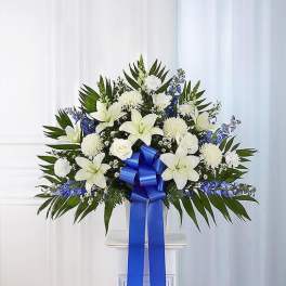 White lilies and blue flowers arranged with a large blue ribbon