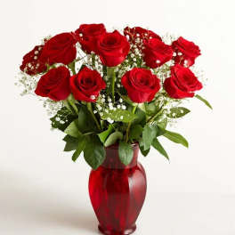 Red roses arranged in a red glass vase with baby's breath