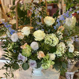 Large mixed floral arrangement in a white vase with roses and blue blossoms