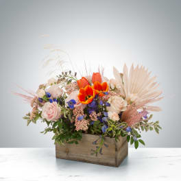 Rustic wooden box arrangement with orange tulips, blush roses, blue flowers, and dried palm and grasses