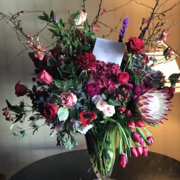 Large mixed bouquet in a clear glass vase with red, pink, and white blooms