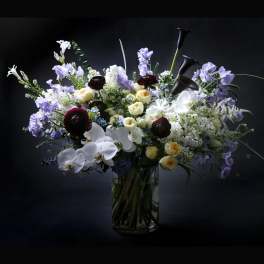 Mixed bouquet of white, lavender, and dark red flowers in a glass vase