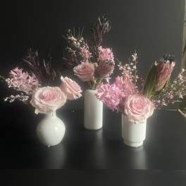 Three small pink floral arrangements in white vases on a dark surface