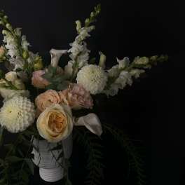 Soft peach and white flowers arranged in a white vase against a dark background.