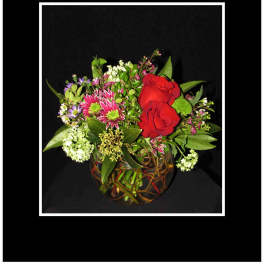 Red roses and mixed flowers arranged in a round glass vase