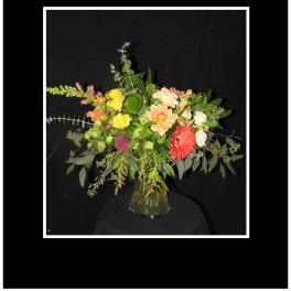 Mixed bouquet in a clear glass vase with yellow, peach, red, and white blooms