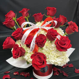 Red roses arranged in a red hatbox with white hydrangeas and ribbon