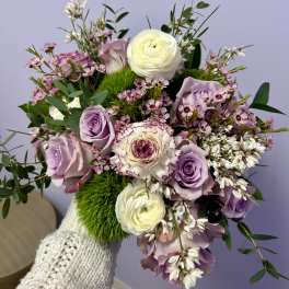 Handheld bouquet of lavender roses, white ranunculus, and pink blooms