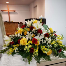 Large casket spray with white lilies, red and yellow roses, and yellow flowers