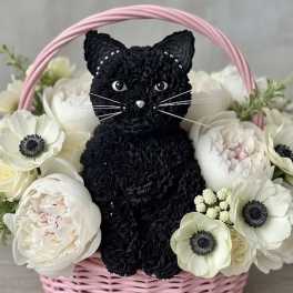 Black cat figure in a pink basket surrounded by white flowers