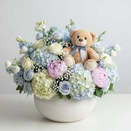 Pastel flower arrangement in a white bowl with a teddy bear