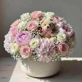 Pink and white flower arrangement with a teddy bear in a white bowl vase