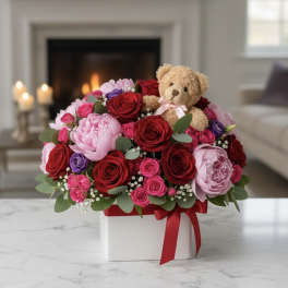 Bouquet of red, pink, and purple roses with a teddy bear in a white box
