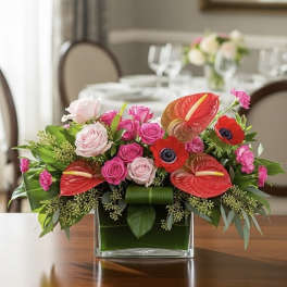 Pink roses and red anthuriums arranged in a clear square vase