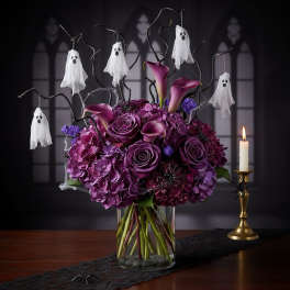 Purple floral arrangement with hanging ghost decorations in a glass vase