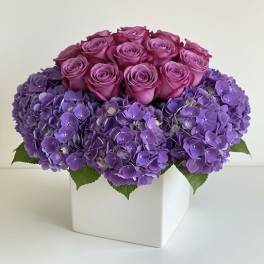 Pink roses and purple hydrangeas in a white square vase