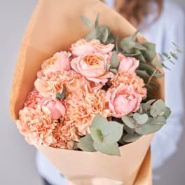 Bouquet of pink roses and peach carnations wrapped in brown paper