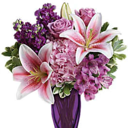 Pink lilies and purple flowers arranged in a tall purple vase
