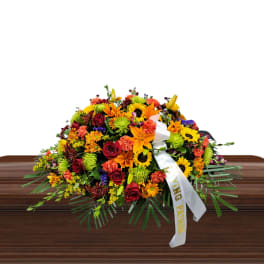 Large mixed flower spray with a white ribbon on a wooden casket