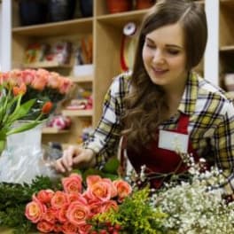 Florist arranging pink roses and mixed flowers at a worktable