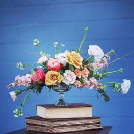 Mixed roses and ranunculus in a silver compote on stacked books