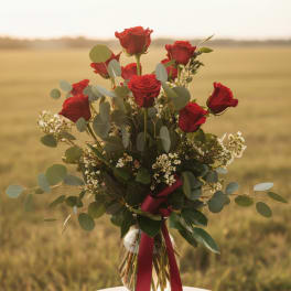 Red roses in a glass vase with greenery and a burgundy ribbon