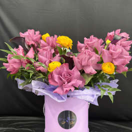 Pink roses and yellow ranunculus in a lavender hat box